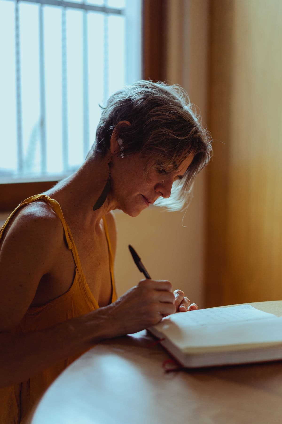 A woman writing in a notebook beside a sunlit window