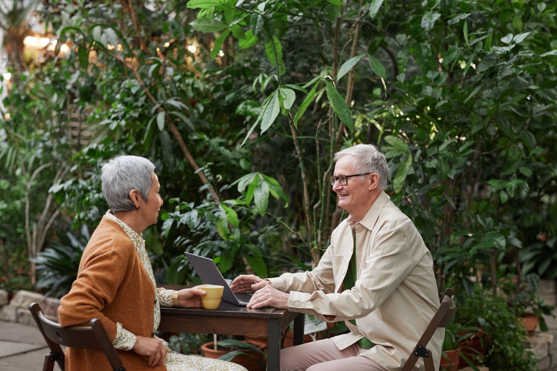 An older couple enjoying coffee and conversation in a leafy garden